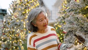 Elderly asian couple embraces near a beautifully decorated Christmas tree. The husband places a warm scarf around his wife, filling the air with love and festive cheer as they share joyful smiles. - Powered by Shutterstock - Get 15% off with code: PIKWIZARD15