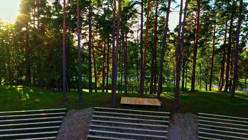 Wooden stage and bench seating in forest clearing with sunbeams shining through trees in Smiltene, Latvia