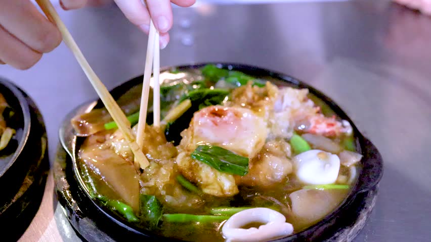 Hand uses chopsticks to pick up seafood pad thai noodles from a sizzling hot plate.