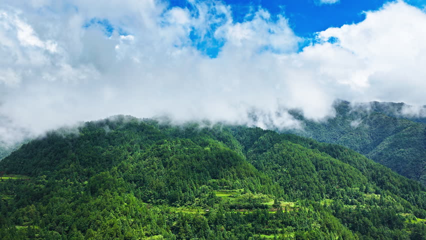Aerial shot of beautiful green mountain landscape with dense forest and clouds under blue sky