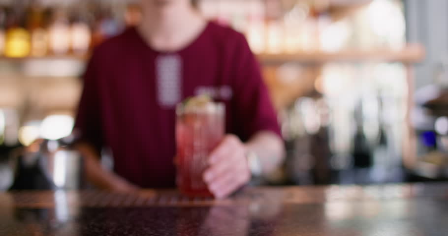 Barkeeper work. Making beverage. Worker adding straw to tall glass with red ice juice mix. Flavored citrus mint cold cocktail on pub table.