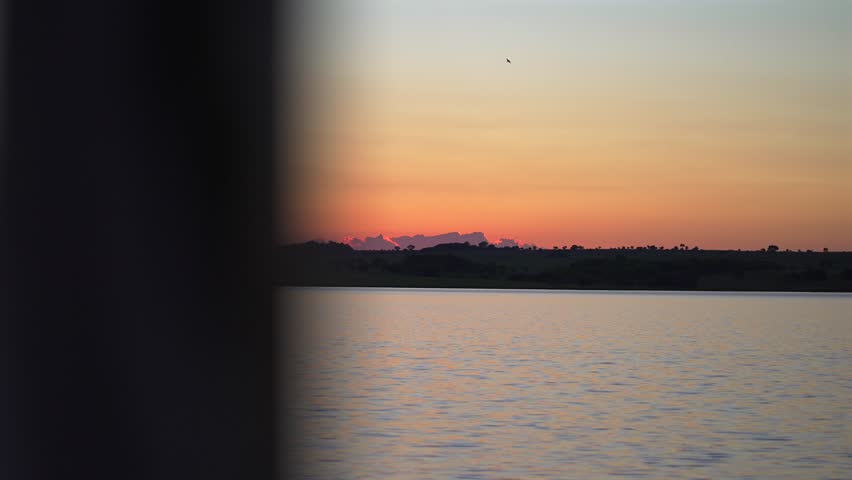Wide shot of the sun setting over the calm water of the Paraná River, Argentina, with palm tree silhouettes and golden reflections.
