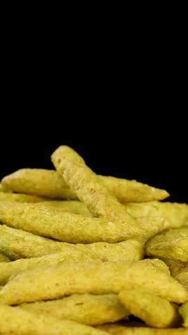 Human hand picks green pea puffed snack sticks under studio lighting, close-up, black background