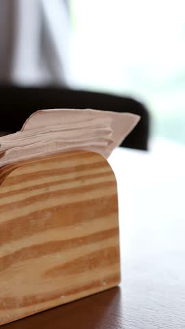 Close-up of personâs hand pulling paper napkin from wooden holder on cafe table