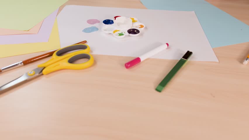 Hand mixes vibrant watercolor paints on palette, overhead view, soft lighting, art supplies visible