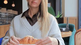 A woman sits at a table in a modern cafe, gently breaking a fresh almond croissant. Warm light, wooden interiors, and green plants create a calm and cozy atmosphere. - Powered by Shutterstock - Get 15% off with code: PIKWIZARD15