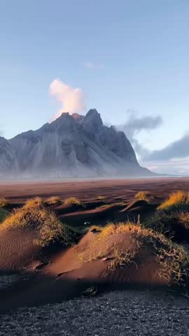 A dramatic view of a smoking volcano surrounded by rugged terrain and dynamic weather, perfect for cinematic projects.