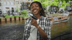 African american woman holds electric drill in hand and smiles on street by canal in amsterdam; playful confidence. - Powered by Shutterstock - Get 15% off with code: PIKWIZARD15