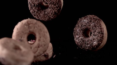 Lots of sweet but sinful iced donuts falling in slow motion and bouncing off each other on a black background.