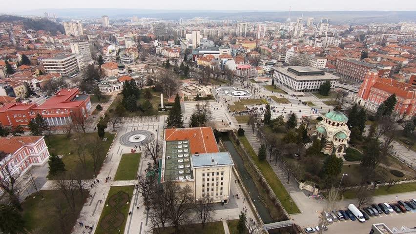 Drone video of Pleven center on March 3, 2019, showing landmarks, the square, the Ossuary, church, municipal building, fountains, and people walking with a long national flag, Pleven, BG,03 March 2019