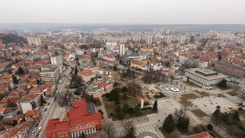 Drone video of Pleven center on March 3, 2019, showing landmarks, the square, the Ossuary, church, municipal building, fountains, and people walking with a long national flag, Pleven, BG,03 March 2019