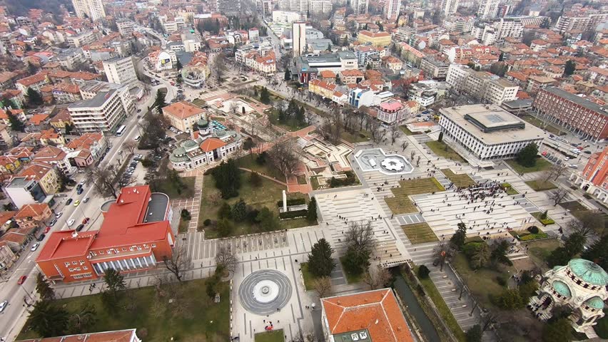 Drone video of Pleven center on March 3, 2019, showing landmarks, the square, the Ossuary, church, municipal building, fountains, and people walking with a long national flag, Pleven, BG,03 March 2019