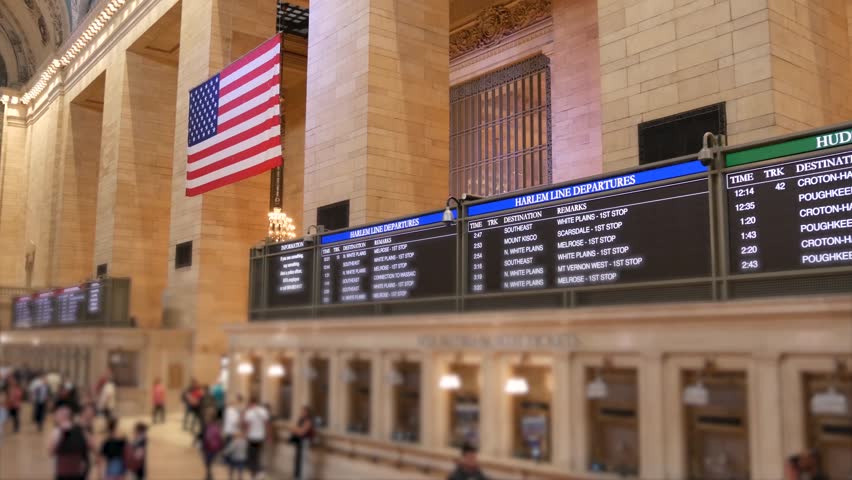 New York Grand Central Terminal on 42 street, United States. Crowd of people inside railway building. American flag, railroad transportation in Manhattan Midtown, NYC. Station interior and passengers.