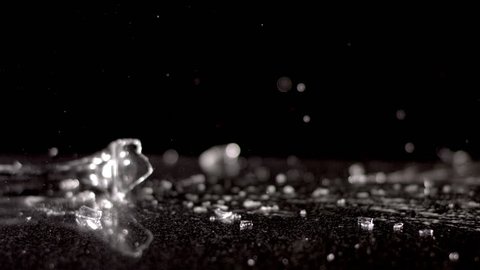 A champagne glass falls in slow motion against a black background. It shatters as it hits the ground, spilling its contents and sending shards of glass flying everywhere.