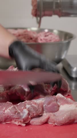 Vertical video. Cook uses knife to cut meat on table in kitchen of production facility