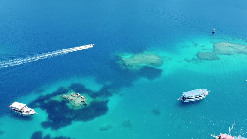 Aerial drone view showing boats moving above coral reefs near Suluada Island in clear blue sea, perfect for Social Media travel content and bright tropical style coastal scenes.
