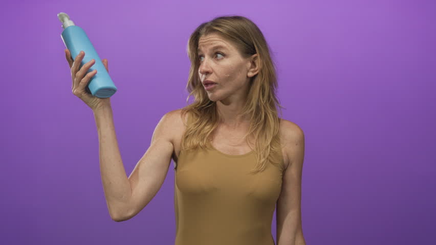 Woman holding two shampoo bottles while shrugging and comparing products in a purple studio backdrop; indecision choice comparison.