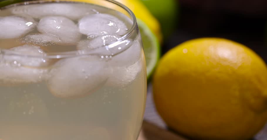 cold lemon drink with pieces of pure ice in a glass, sweet and sour refreshing drink with lemon flavor and whole juicy lemons and limes