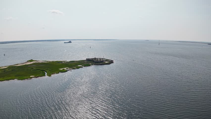 Aerial footage shows a small dock and green island in the calm waters of Charleston Harbor, with boats and ships visible on the horizon.