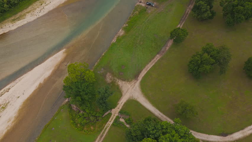 Open sand dirt road and grassy fields beside wooded lake hills with boat in distance, Tagg Flats, Lake Eucha Oklahoma USA, drone tilt up establish