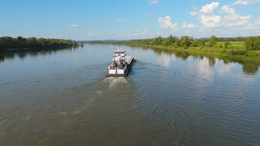Aerial rearview of small boat barge cruising down calm Arkansas river surrounded by lush riverbank greenery