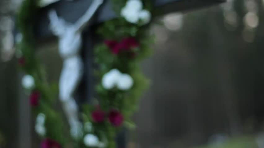 Detailed close-up of a silver figure of Jesus Christ on a wooden crucifix, beautifully decorated with fresh green garlands and white and red flowers during an outdoor religious ceremony.