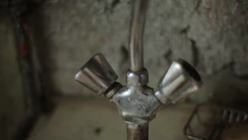 Close-up shot of an old, dirty, and worn metal water faucet in a rustic setting, with a large amount of hot steam or vapor rising around it, suggesting extreme heat or malfunction.