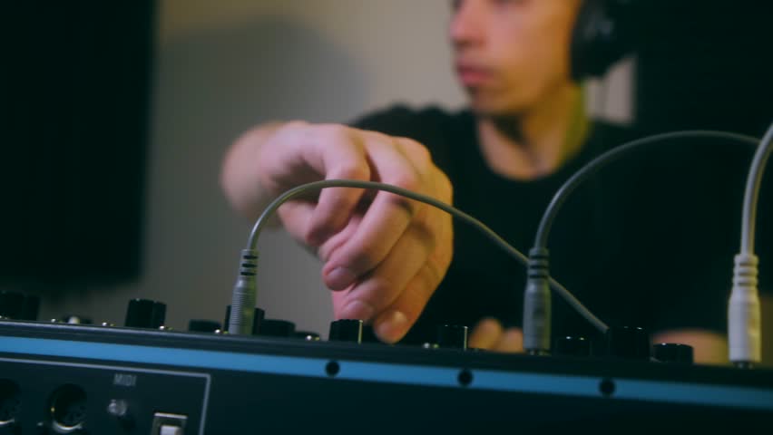 Young sound producer with headphones adjusting the knobs on a professional audio mixing console, creating a new electronic music track in a recording studio with a creative atmosphere. Creating music.