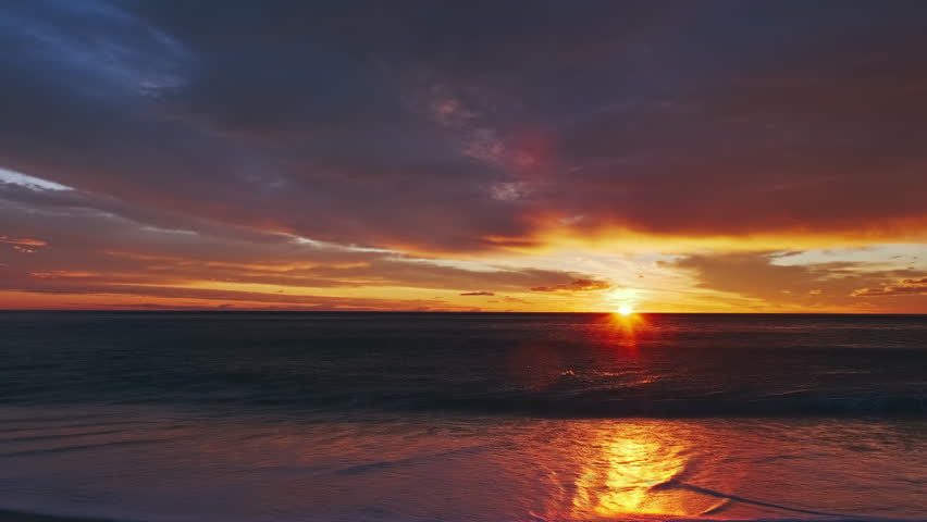 Sunset over sea with vibrant red and orange sky reflecting on water and shore. Beautiful seascape time lapse, 4k