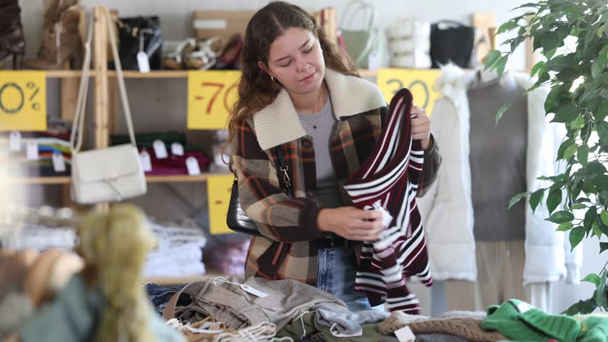 Selective young woman choosing winter jersey in clothing shop with large assortment