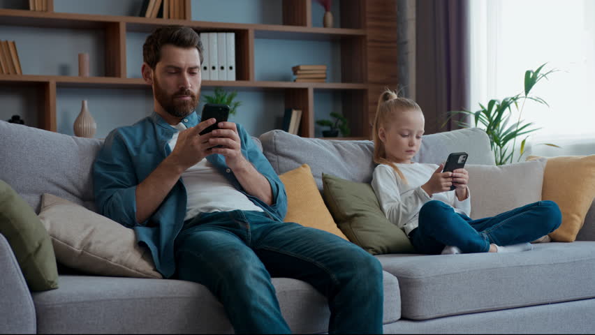 Caucasian family internet addicted at home father with daughter looking phones typing chatting social media playing virtual game mobile apps overuse dad with child kid girl focused with smartphones