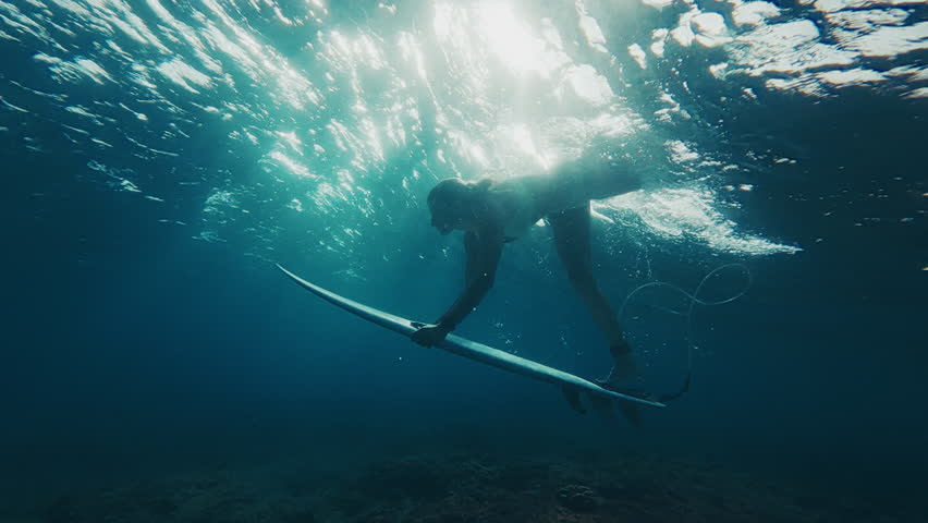 Woman surfer in bikini dives under the ocean wave with surfing board and passes it. Underwater view of the surfer doing duck dive trick