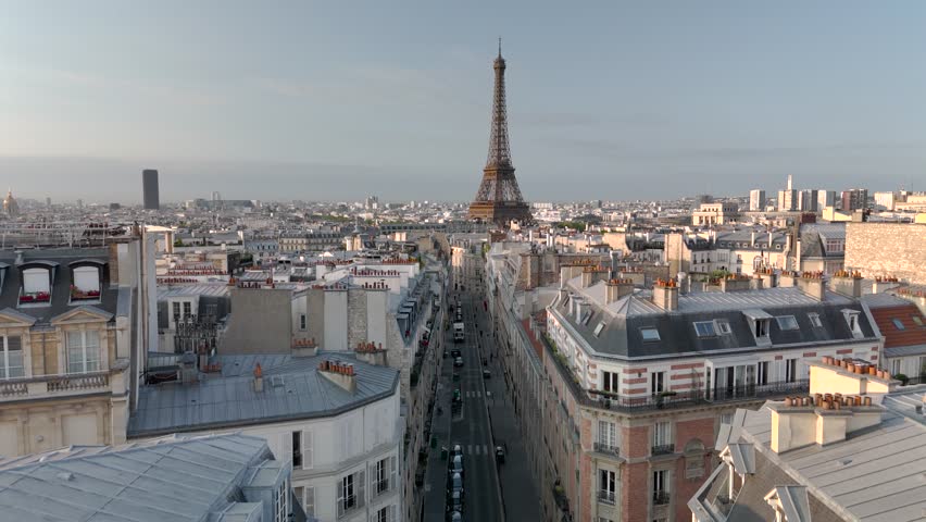 Aerial drone view of the sleepy streets of Paris, France, overlooking the famous Eiffel Tower and Champ de Mars at sunrise or sunset. Low motion over the rooftops. Cinematic 4k. Europe from above.