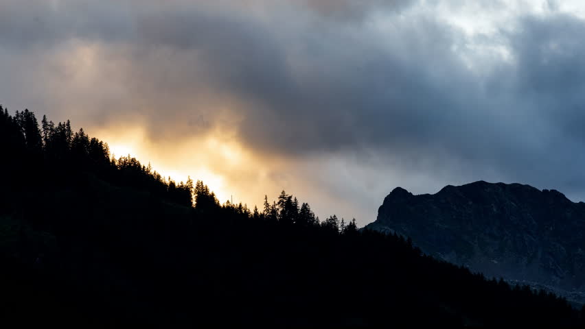 Clouds drift over a serene forest and mountain backdrop at dusk, timelapse