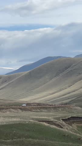 Car on a scenic mountain road under a cloudy sky, traversing vast rolling hills and distant peaks. Armenia, Yerevan 15.04.2023