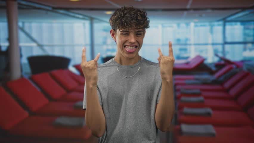 Teenager makes rock sign with hands in airport lounge with red recliners; youthful playful confidence.