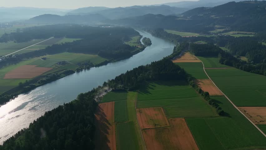 Summer drone footage of Drava river near Gortina, green slopes, calm water, valley curves, soft evening light, peaceful aerial movement