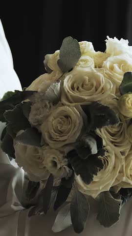 Vertical video. Bride holding a wedding bouquet of white roses and greenery, wedding morning in a hotel room. Slow motion.