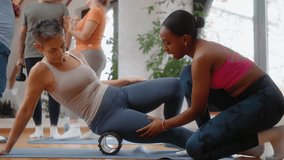 Black female instructor assisting an older woman during a foam roller exercise, creating a positive, relaxed, and joyful atmosphere in a senior group fitness class. - Powered by Shutterstock - Get 15% off with code: PIKWIZARD15