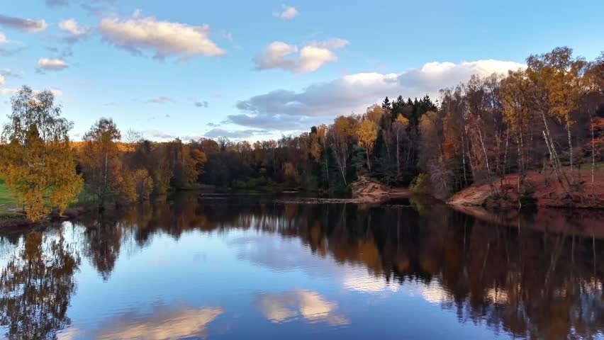 calm pond mirror under blue sky, still water reflecting cotton clouds and golden treeline, clear horizon line,