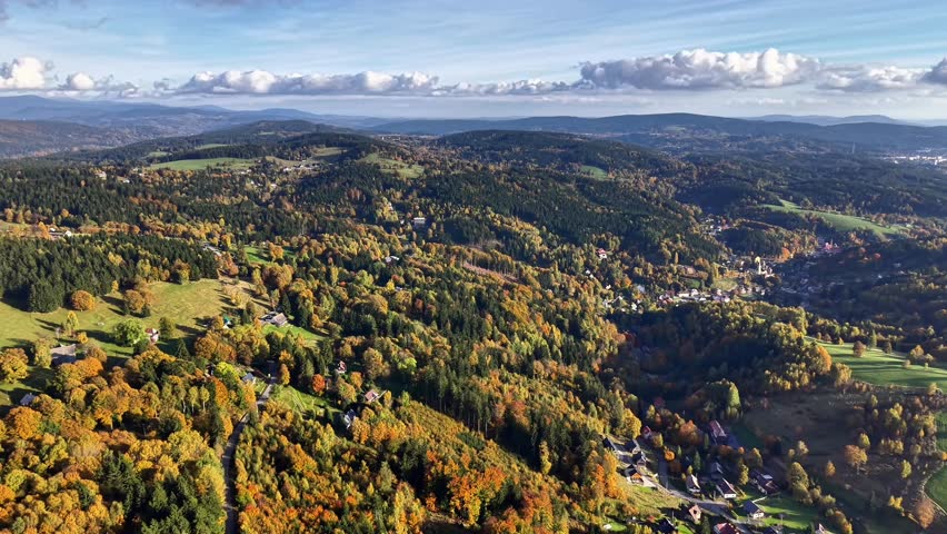 aerial hillside mosaic of autumn villages and mixed forest, colorful patchwork of houses, fields and winding