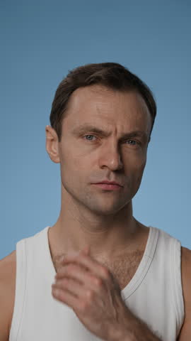 Vertical shot of adult man looking at himself while touching chin and cheeks to check stubble