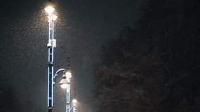 Heavy snow falling at night, illuminated by a row of modern streetlights with blue neon accents, creating a serene and magical winter atmosphere in a quiet city park or street - Powered by Shutterstock - Get 15% off with code: PIKWIZARD15