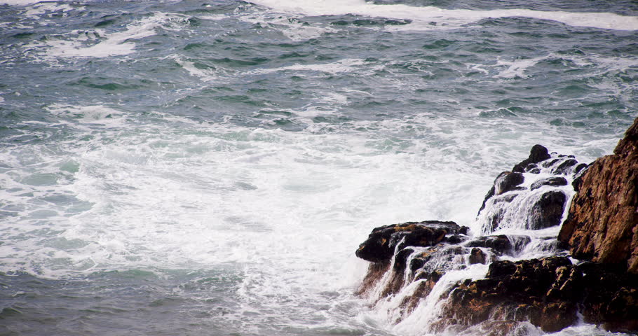 Panorama of ocean surf hitting sharp rocks.