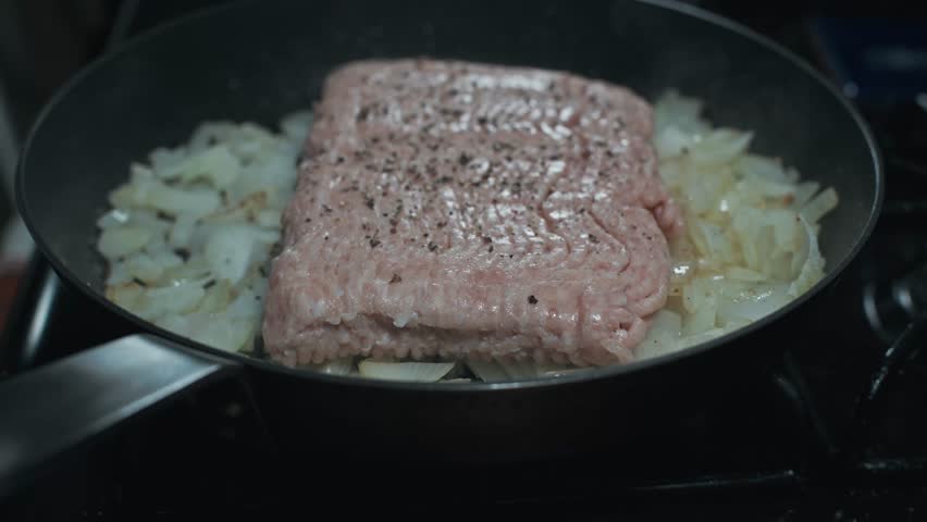 Adding Seasoning to Raw Meat and Onions Sautéing in a Hot Skillet