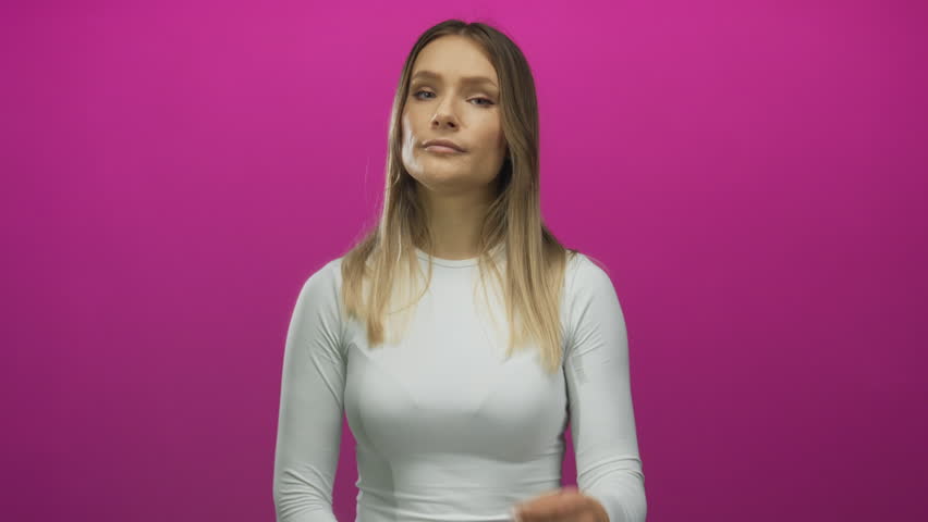 Young woman with long blonde hair poses thoughtfully against a vibrant pink background, wearing a white shirt and expressing contemplation.