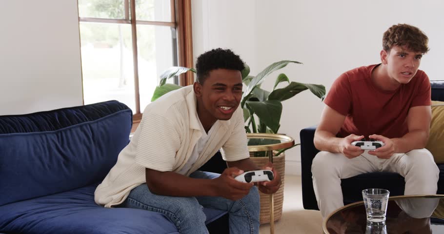 Two men starting gameplay on couch holding pads blue reaction icons appearing seeking engagement. Gaming, friends, livingroom, console, controllers, sofa, armchair