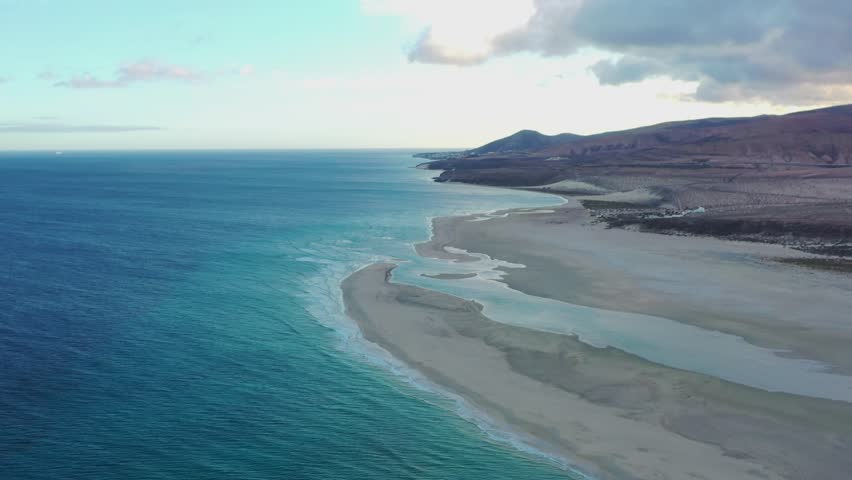Drone footage capturing the serene sunset colors reflecting over the coastline of La Barca Beach, highlighting its natural beauty and peaceful atmosphere.