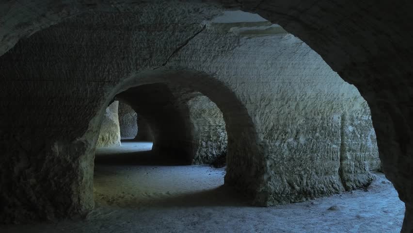 Caucasian man in his 50s examining the cave from the outside to plan a tourist expedition in Natural cave chalk mines passage through opening to outdoor area dolly camera movement