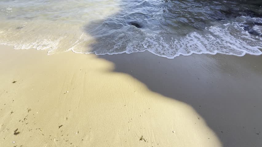 a gorgeous summer landscape at the beach with large rocks in silky brown sand surrounded by blue ocean water and waves rolling into the beach with powerful clouds at sunset at Leadbetter Beach 